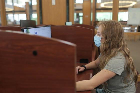 Photo of a female Chatham University student wearing a mask, working on a computer in the library