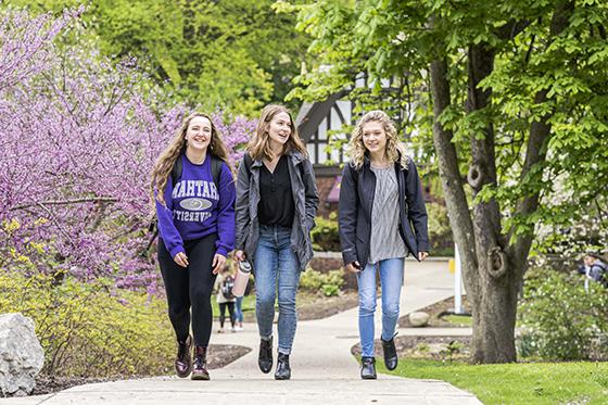 Photo of three female Chatham University walking to class on Shadyside Campus during the spring, with green trees on colorful blossoms. 